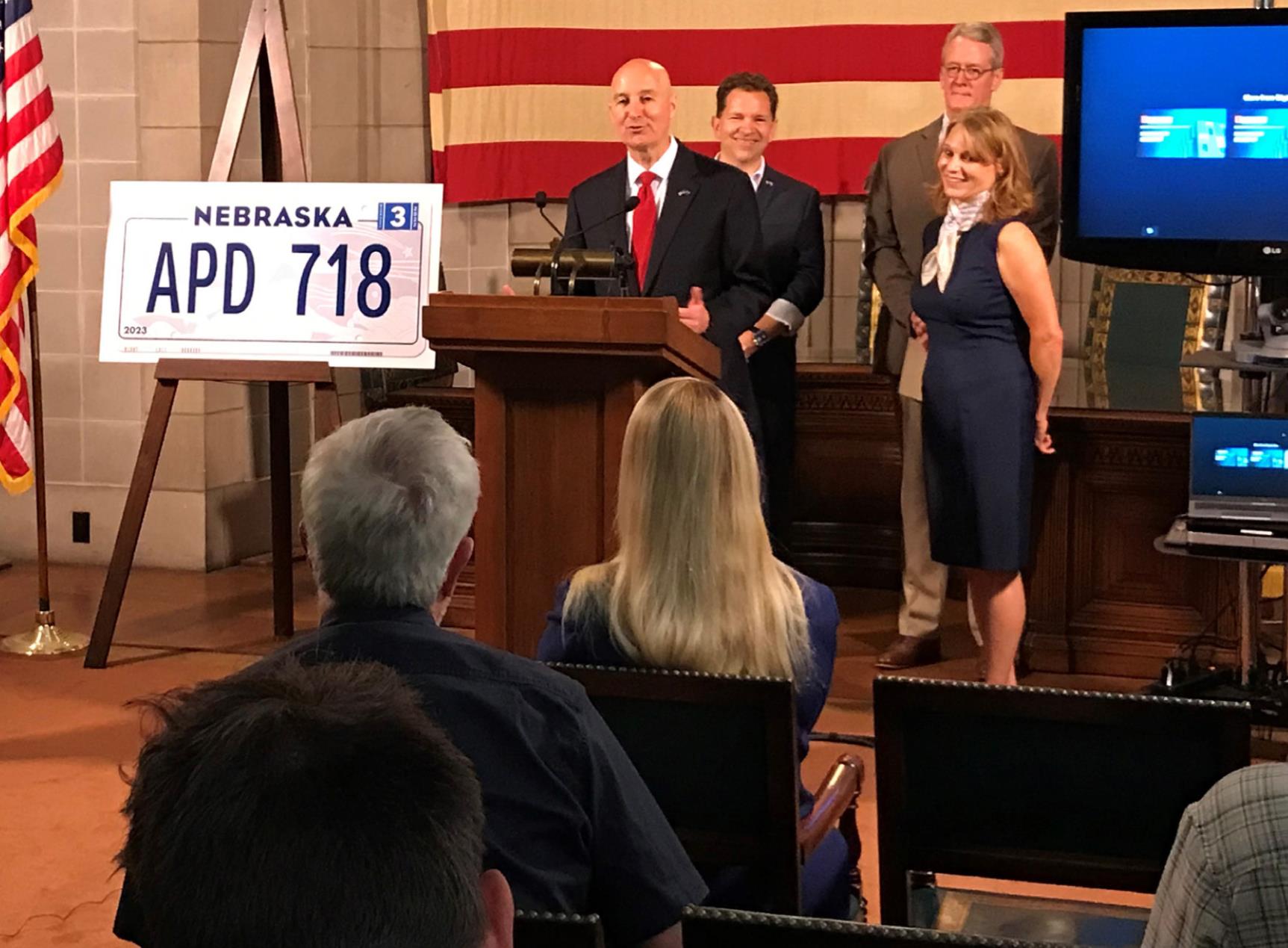 Gov. Ricketts (podium) announced the new Nebraska license plate design Tuesday. He was joined by Drew Davies (right of Gov. Ricketts); First Lady Susanne Shore (front right) and Capitol Administrator Bob Ripley (back right) for the announcement.