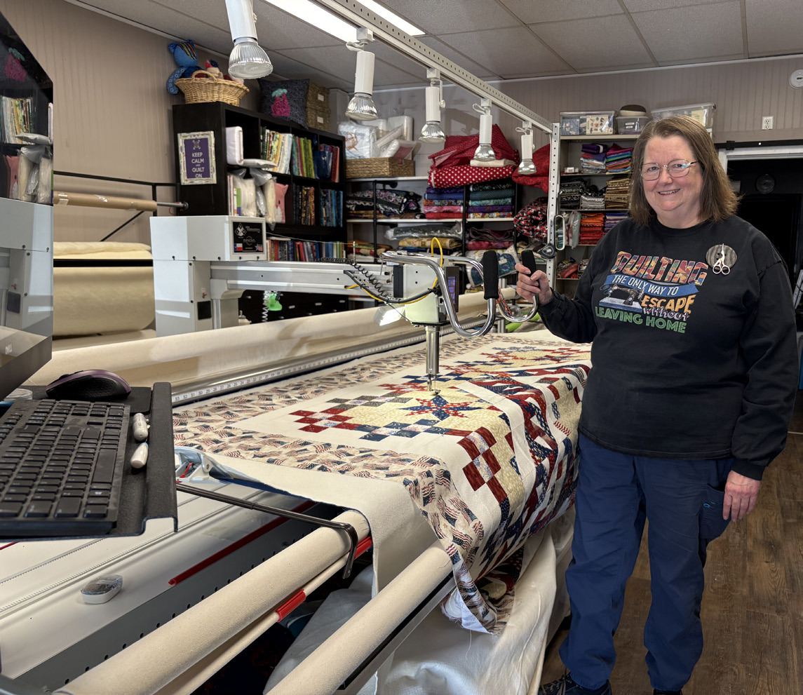 Kristina Morrow (pictured) programs the computer (at the left) and this machine quilts out the pattern. PCN photo by Beth Sparrow.