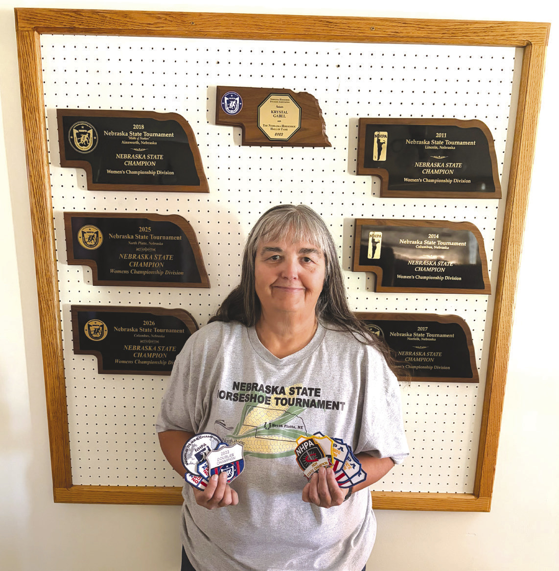 Above: Krystal Gabel of Shelby is pictured with her many plaques in horseshoes, including state champion for six years. She also holds patches of her other accomplishments. Photo provided.