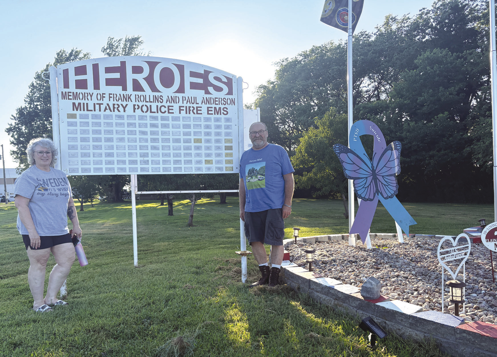 Above: Paula Rollins and Dave Rollins stand by the Heroes Wall they’ve put up on their property. Below: Their display currently shows the cross at its center with the American flags and others. The pink heart is for cancer and dementia and the blue/purple ribbon for suicide and PTSD.