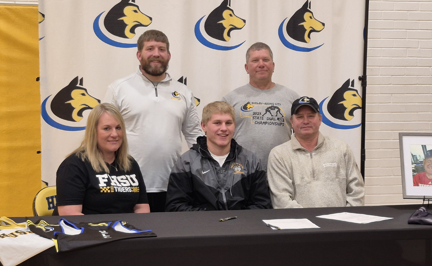 Shelby-RC Huskies senior Eli Fjell, front-middle with his mom Jen to his right and his dad Ryan to his left signed his letter of intent to attend Fort Hayes State University next fall to continue his education in Agriculture and wrestle for the FHSU Tiger’s wrestling program. Back row L-R is SRC head coach Tanner Kuhn and assistant coach Chris Watts. PCN photo by Ken Kush.