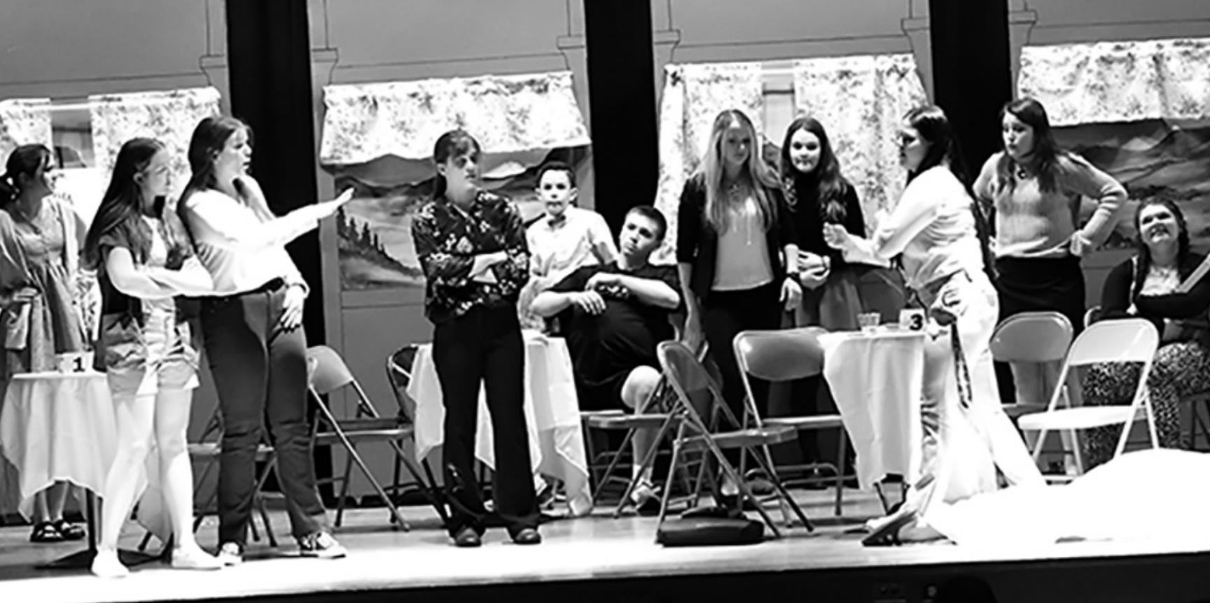 Doctor Lauren Maloney (Caydee Bauers) defends herself against accusations of murder with enthusiastic vet tech Abby Wells (Mackenzie Kuns) at her side, while pharmaceutical CEO Avery Millen (Cassandra Ziemba) steps over the first murder victim on her way to argue her case. Other characters look on as everyone wonders “whodunnit” in “Murder on the 518”.