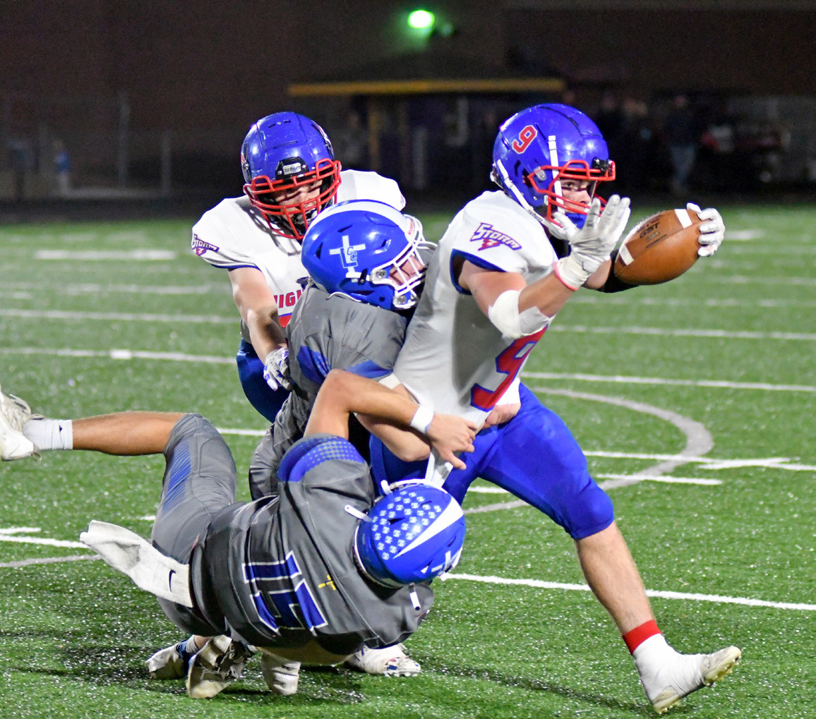 Wyatt Urkoski carries the ball down field while being tackled by two Knight defenders. Photo courtesy of Richard Rhoden of Aurora News-Register.