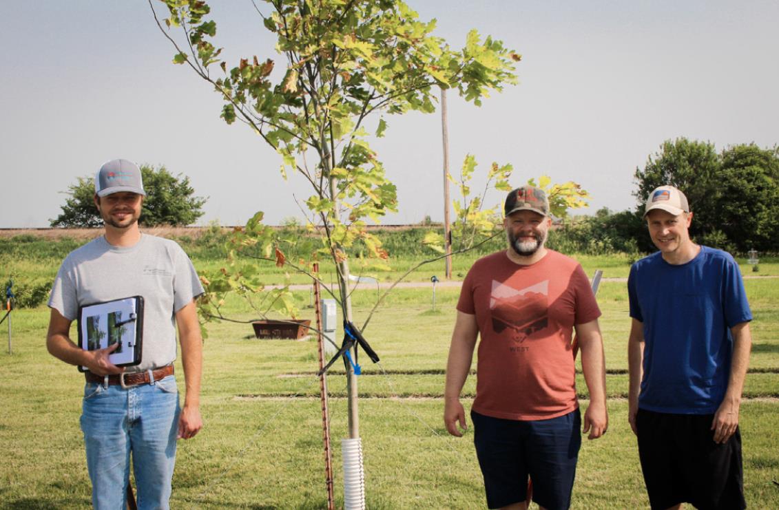 District forester Kyle Yrkoski poses with an anniversary tree planted at Stromsburg’s Buckley Park campground with local park goers Craig Ruskamp and Travis Lindburg. Photo provided by Upper Big Blue NRD.