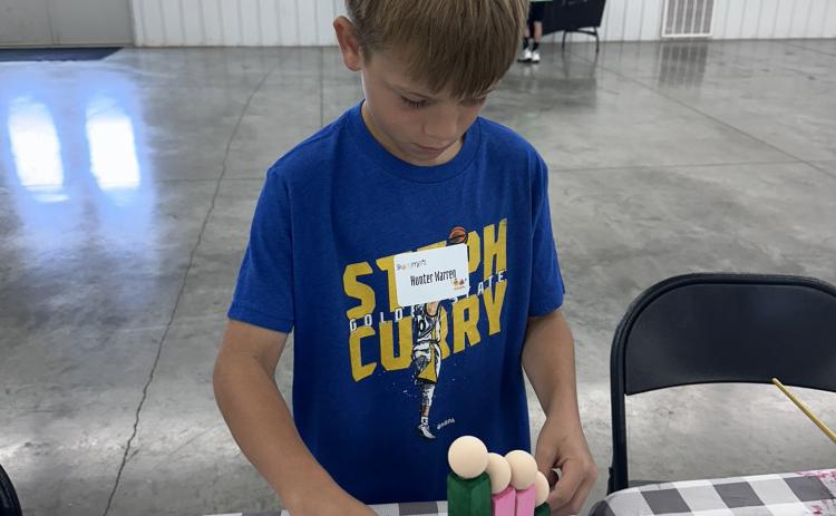 4-H kids have been completing projects. This lad is making a wooden family resembling his. Photo was provided.