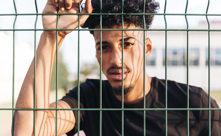A young man behind fence, perhaps at a correctional facility. These services should prevent this. Graphic provided.
