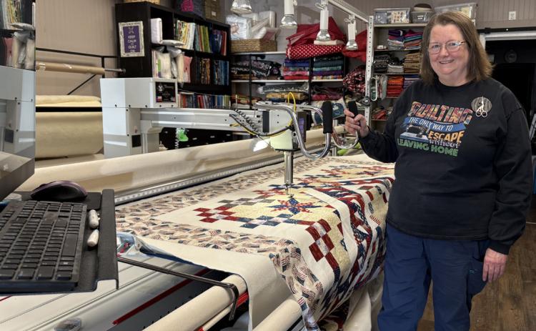 Kristina Morrow (pictured) programs the computer (at the left) and this machine quilts out the pattern. PCN photo by Beth Sparrow.