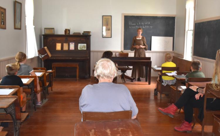 Above: Osceola fourth graders learn fromAlena Mentink at the old one-room school at the museum. PCN photo by Beth Sparrow. Below: Cross County fourth graders tour the Mickey House while Bob Greenwall shows them the photos of notable Nebraskans of Polk County. Photo provided.