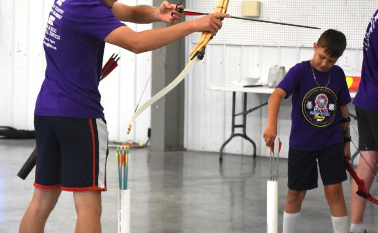 4-H student Bridger Johnson (left) shoots in archery. Johnson was awarded purple and the grand champion in bare bow and recurve; Miller received a blue in bare bow. PCN photos by Beth Sparrow.