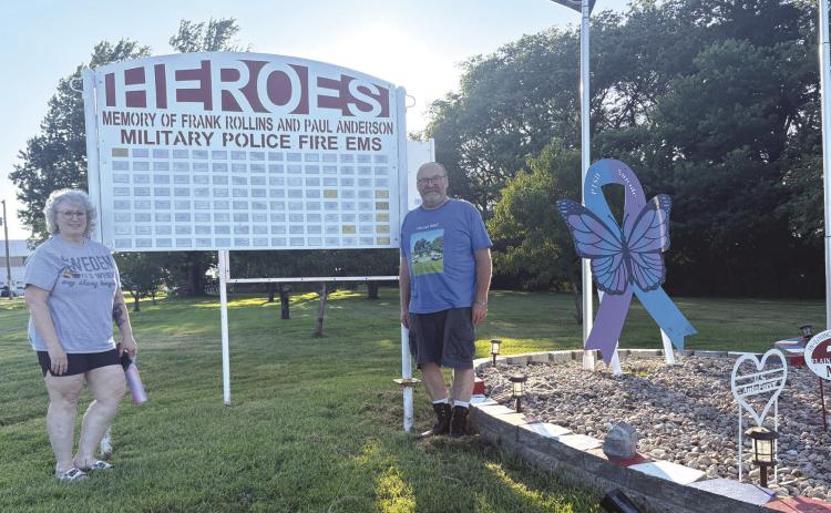 Above: Paula Rollins and Dave Rollins stand by the Heroes Wall they’ve put up on their property. Below: Their display currently shows the cross at its center with the American flags and others. The pink heart is for cancer and dementia and the blue/purple ribbon for suicide and PTSD.