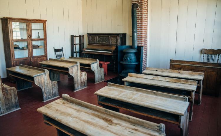 (Left) The inside of a country school often looked something like this. The desks, wood burning stove, piano, teacher’s desk and handbell were staples of the one-room school. Photo provided.