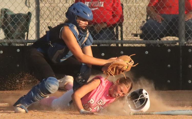 Polk County Slammers freshman Chloe Schott gets her helmet knocked off by the Pierce catcher, but scores the tying run in the bottom of the first. PCN photo by Ken Kush